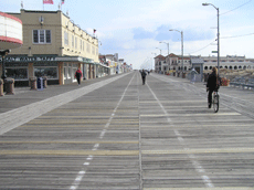 Wooden boardwalk with one person walking in the midground and stores on the left